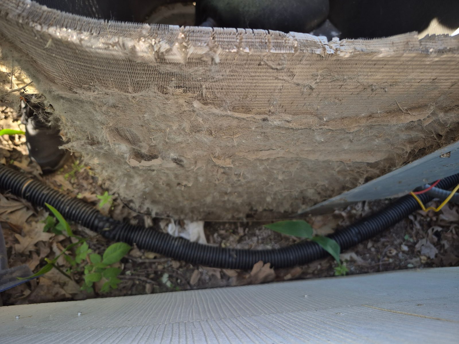 Outdoor AC unit base with thick mat of dust, pet hair and debris choking the bottom coil fins