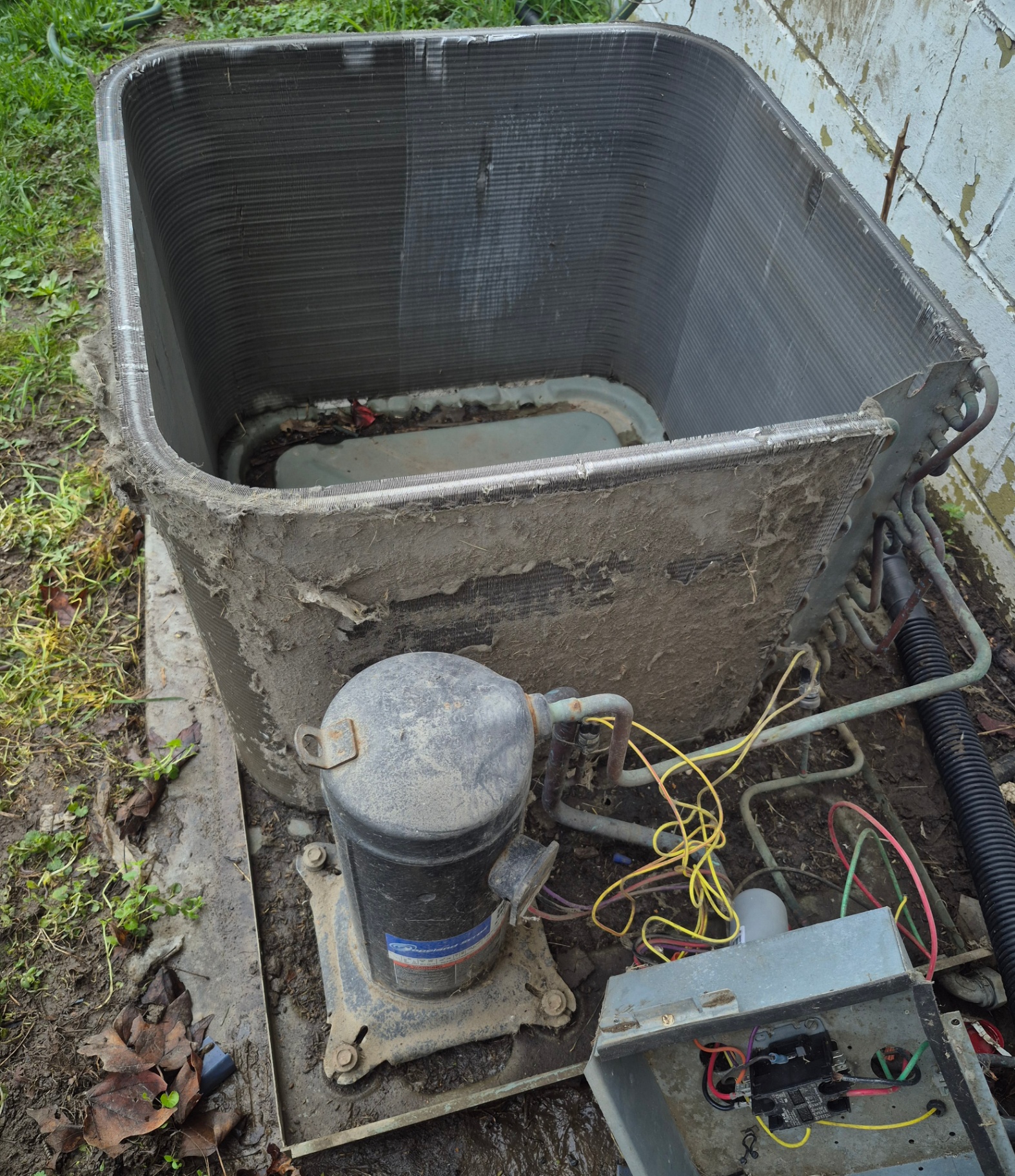 Disassembled outdoor condenser unit caked with dirt and grime around the compressor before service